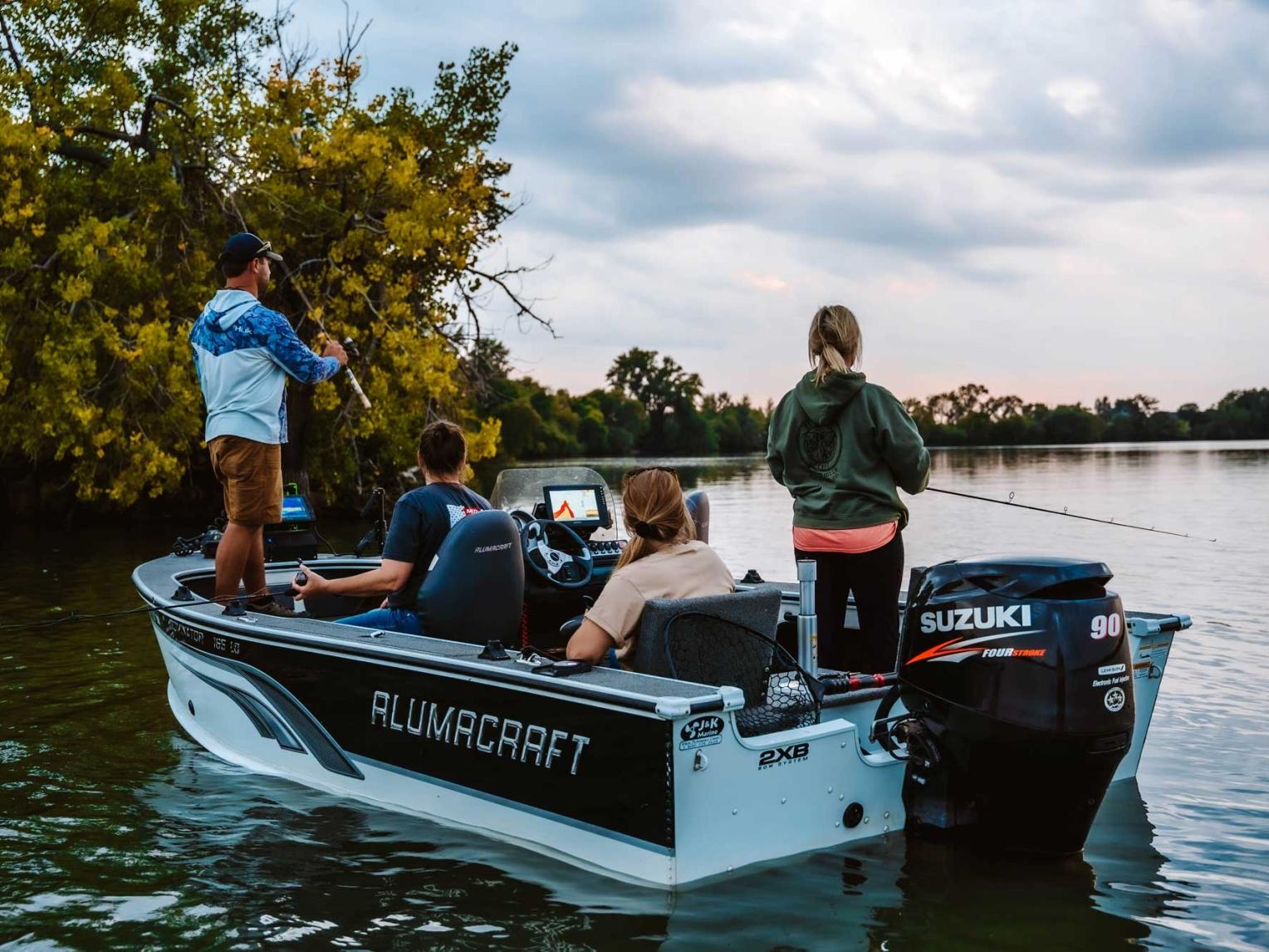 Two men and two women fishing off a motor boat in a lake. They are all facing away from the camera.