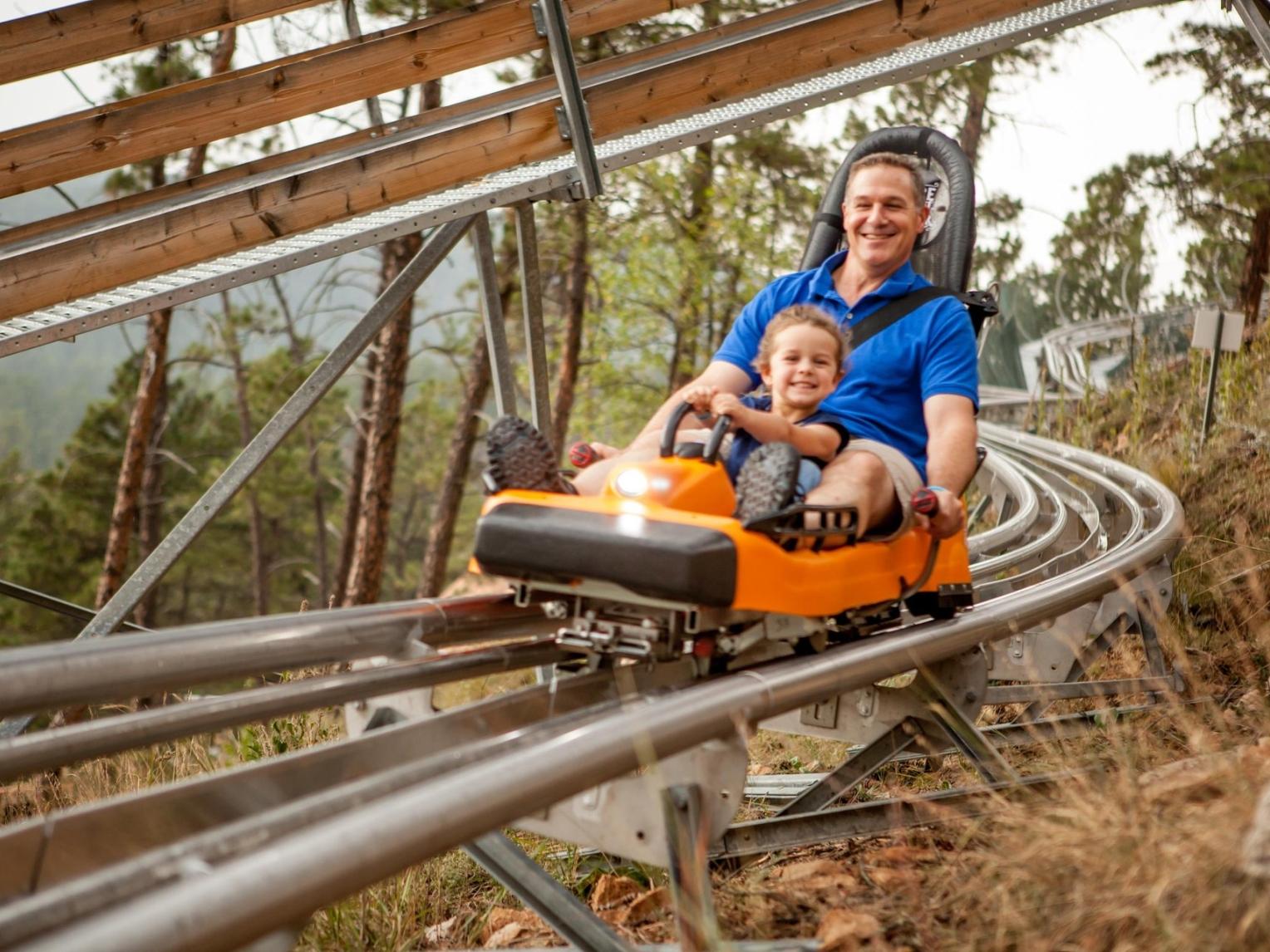 A father and child ride in an orange vehicle on a twisty mountain coaster at Rush Mountain Adventure Park.