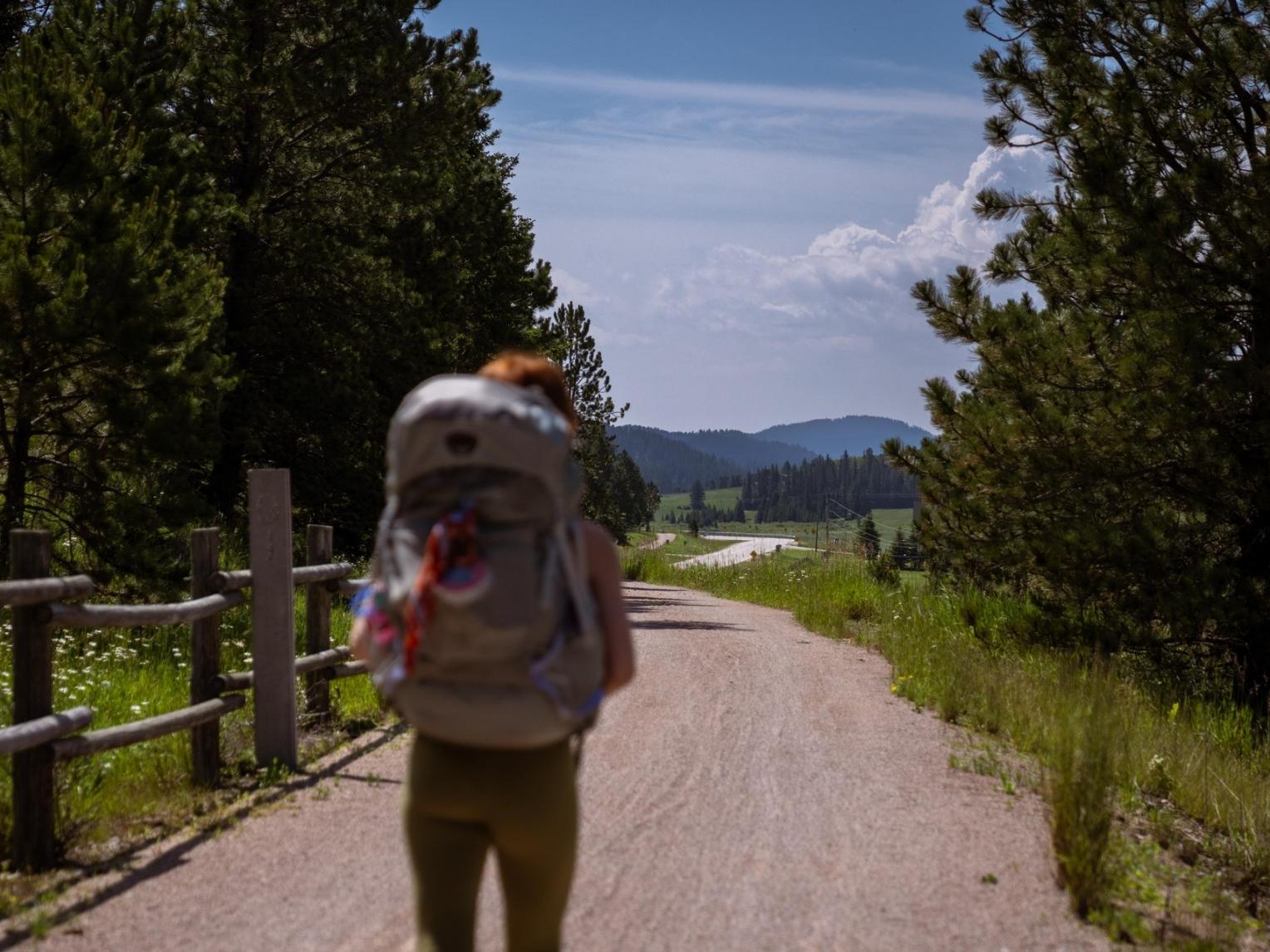 A hiker with a large gray pack stands facing the beautiful Black Hills on the Mickelson Trail.