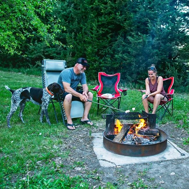 Man, woman and dog gathered around firepit roasting marshmallows