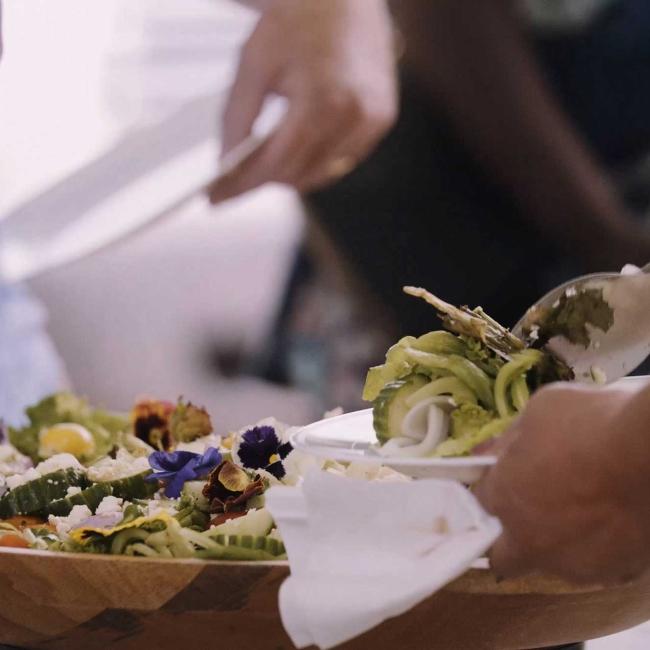 Close up of hands holding a plate while fresh vegetables are being served.