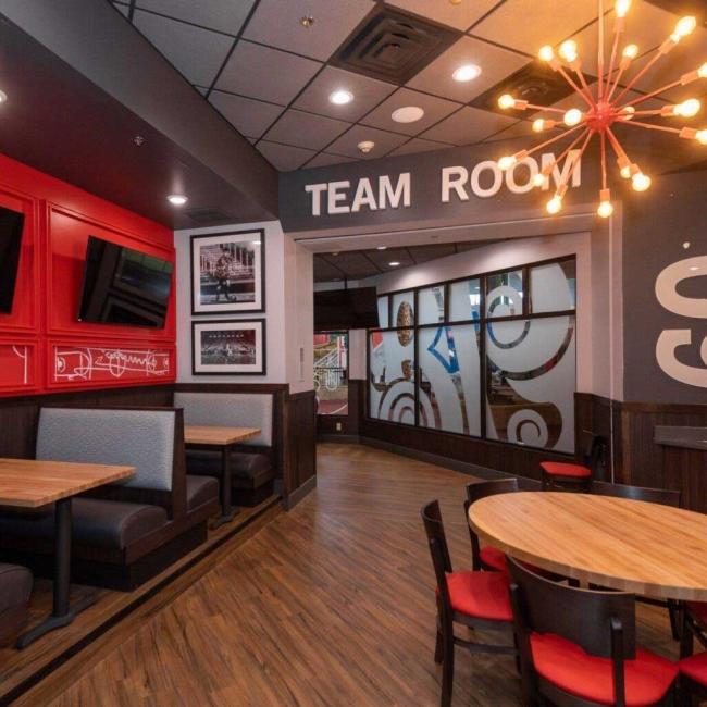 An interior image of Boston's Restaurant at the Ramada Sioux Falls shows a mid-century modern chandelier, booth seating and a large sign that says "Team Room." Sioux Falls, SD.