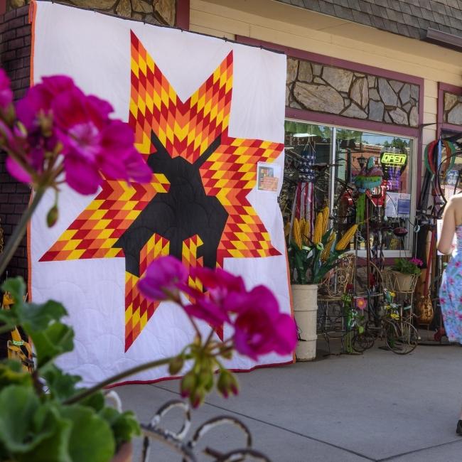 A woman in a floral dress walks by a colorful quilt with a large geometric design in Hill City, South Dakota.