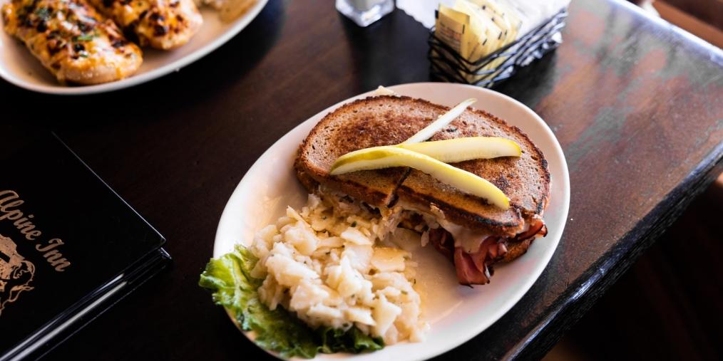 A reuben sandwich topped with slivers of pickle, plus a side of white cabbage, at the Alpine Inn.