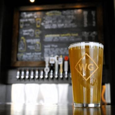 A pint of beer sits in a glass with WG on it at WoodGrain Brewing