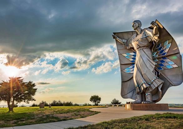 The Dignity statue stands in front of clouds through which the sun shines through