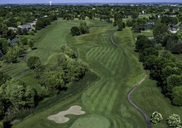 An aerial shot of the Prairie Green Golf Course featuring greens, a sand trap, and a cloudy blue sky