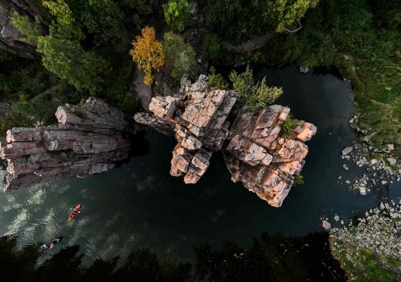 A red kayak and a boat float on the still waters of Split Rock Creek that flows through the towering, geometric quartzite towers of Palisade State Park in South Dakota.