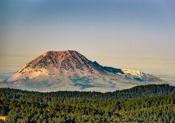 Bear Butte looks like a volcano on a prairie that fades into the distance, framed up front by the nearby Black Hills National Forest.