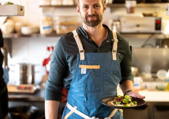 Portrait of Skogen Kitchen in Custer's owner and chef, Joseph Raney with kitchen in the background and finished plates on a vintage green countertop