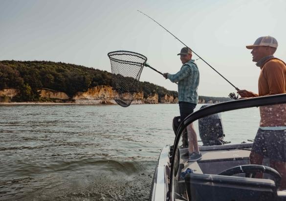 An angler reels in a fish while his friend holds a net from a boat on the waters of South Dakota