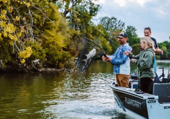 One angler holds a net with a fish as another guides the rod on a boat