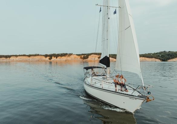 A couple enjoying a moment on a sailboat in smooth waters with the Missouri River bluffs in the background