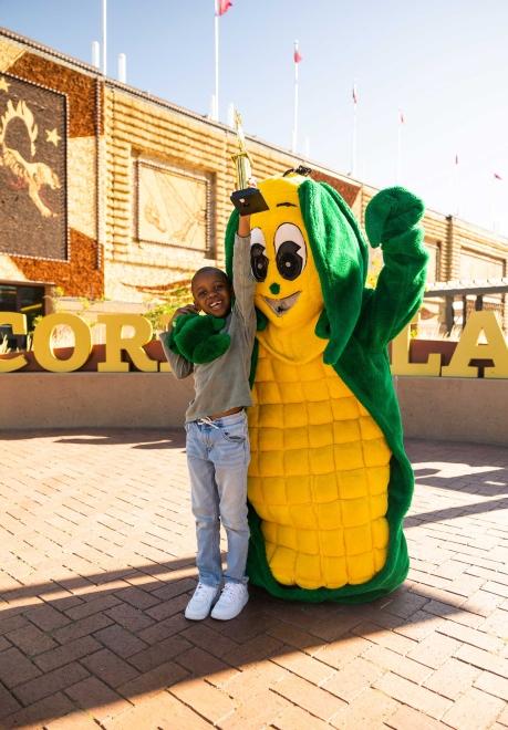 Tariq the "Corn Kid" posing with a Corn Mascot