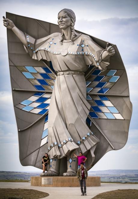 Three people standing in front of Dignity statue