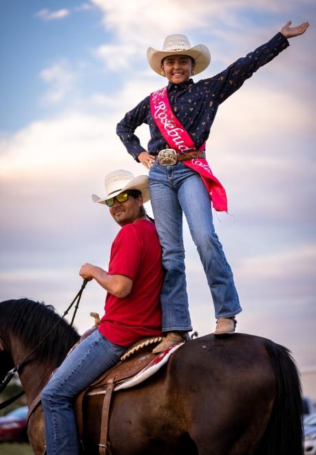 Young cowgirl standing on horse beside rider