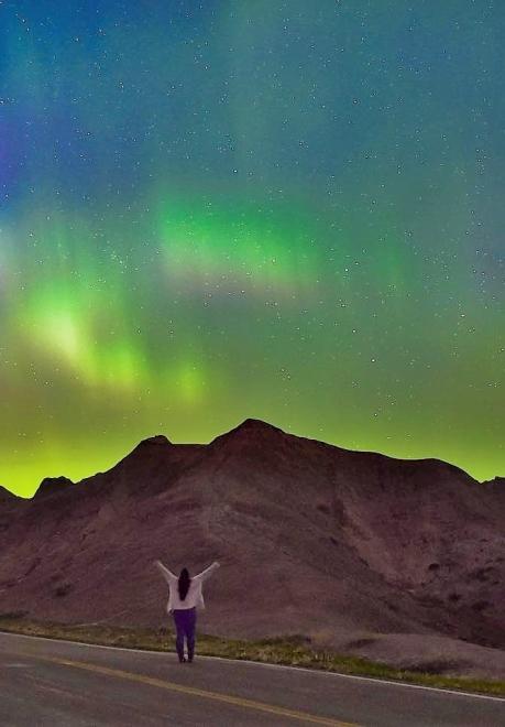 A woman raises her hands in the Badlands under the Northern Lights