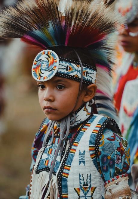 A child stands in full regalia at a powwow