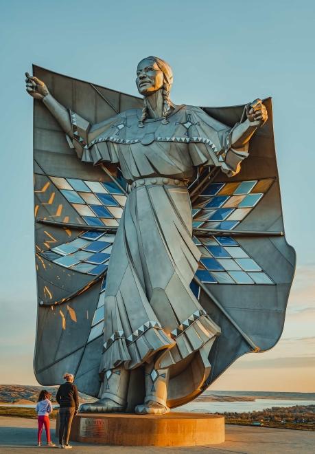 Two people stand to take in the Dignity statue (a Native American woman holding a quilt) near Chamberlain