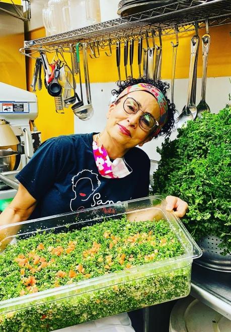 Sanaa holds a large bin of green food at her restaurant