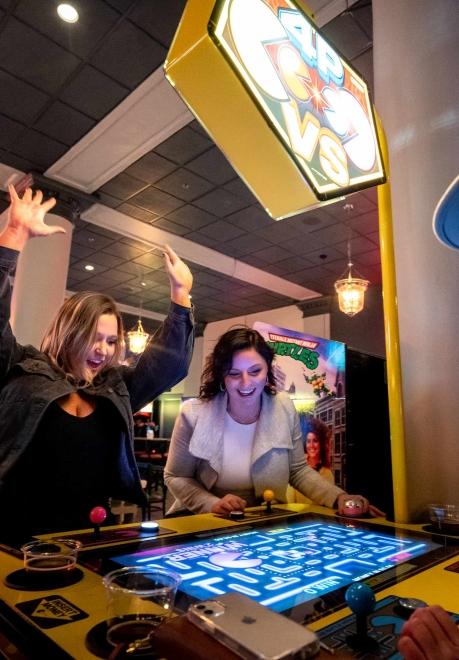 A woman celebrates as another looks on over a game of Pac-Man