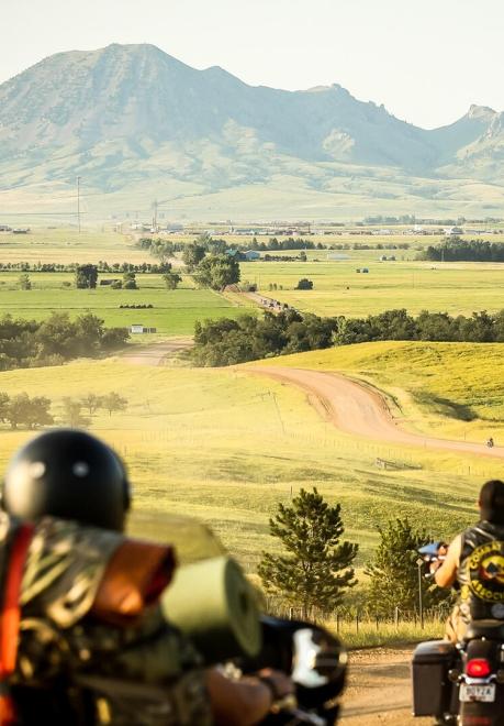 Motorcyclists facing out to a vast landscape with a mountain ahead of them