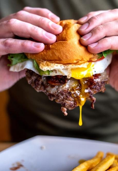 Close of man's hands holding the Fat Smitty Burger with egg yolk dripping off smashed beef patty at Black Hills Burger and Bun in Custer. 