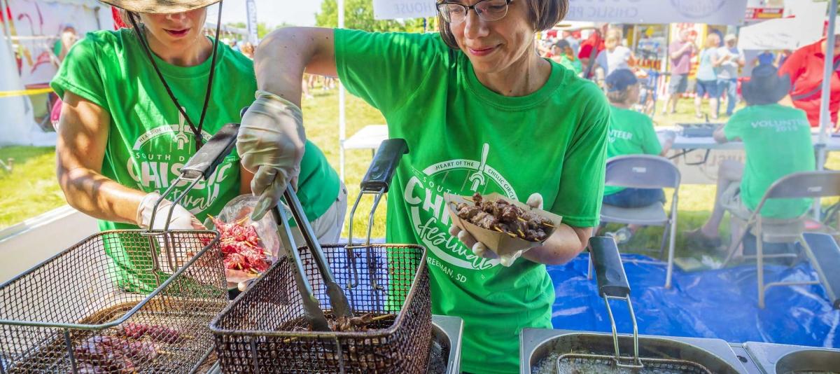 Two women wearing green t-shirts serve chislic at the South Dakota Chislic Festival in Freeman, South Dakota.
