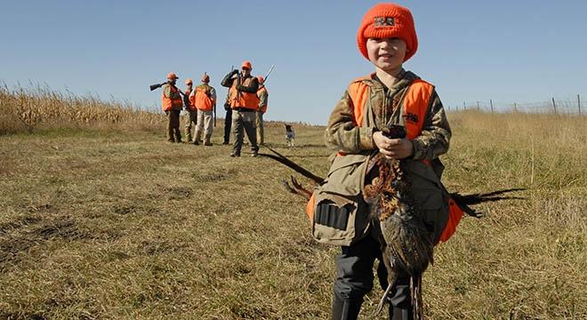 Young hunter holding a pheasant with other hunters in the background